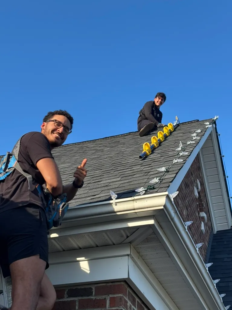 Carlos and a Hang & Glow Crew NC installer clipping C9 Christmas lights along the roofline of a brick home in Cary, NC